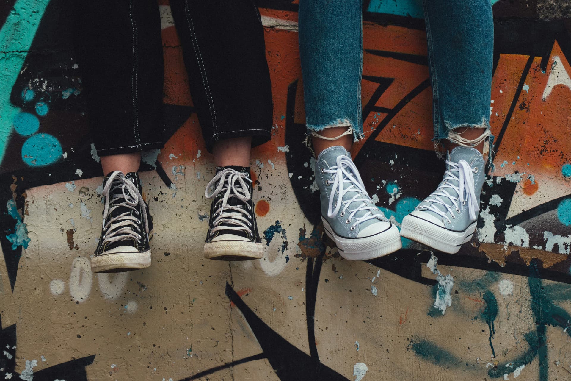 Two pairs of sneakers dangling in front of a graffiti wall.