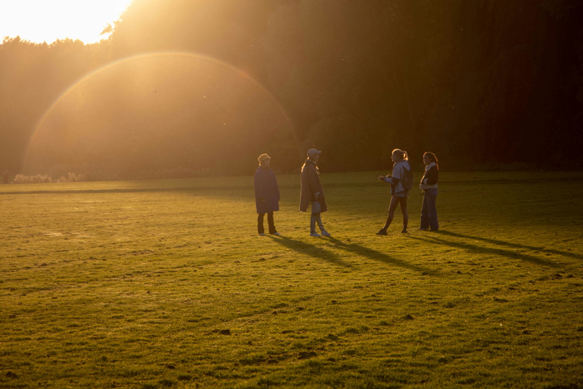 A group of teenagers standing in a wide grassy field at golden hour.