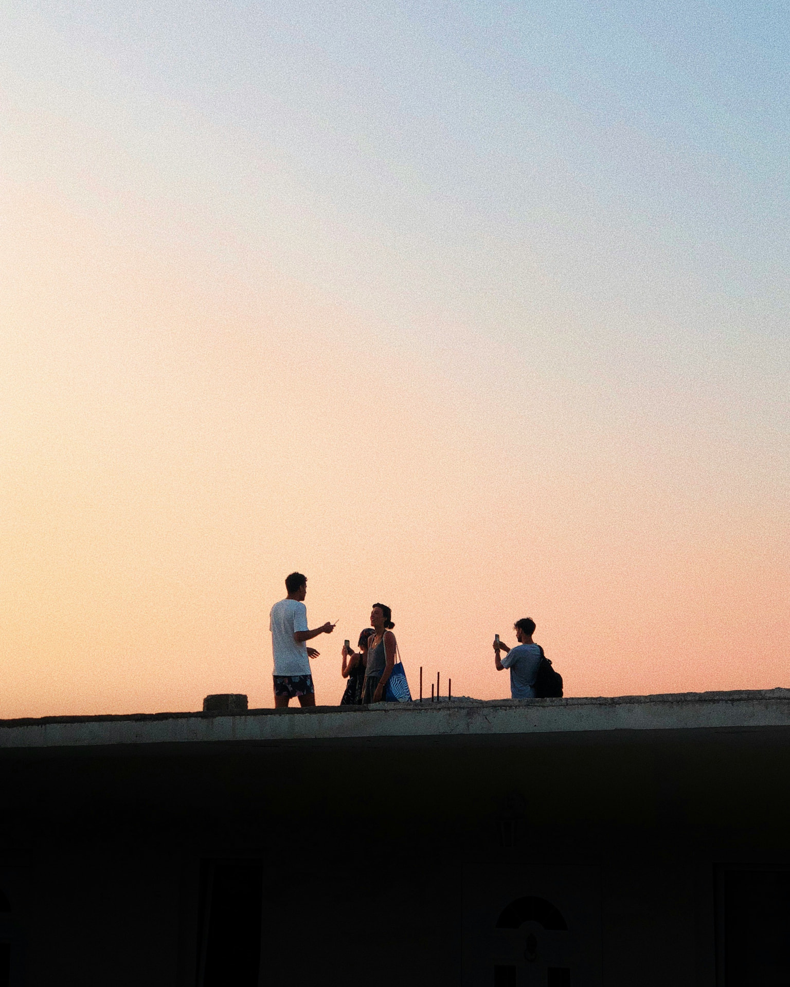 Three young friends on a rooftop at sunset, talking and taking photos.