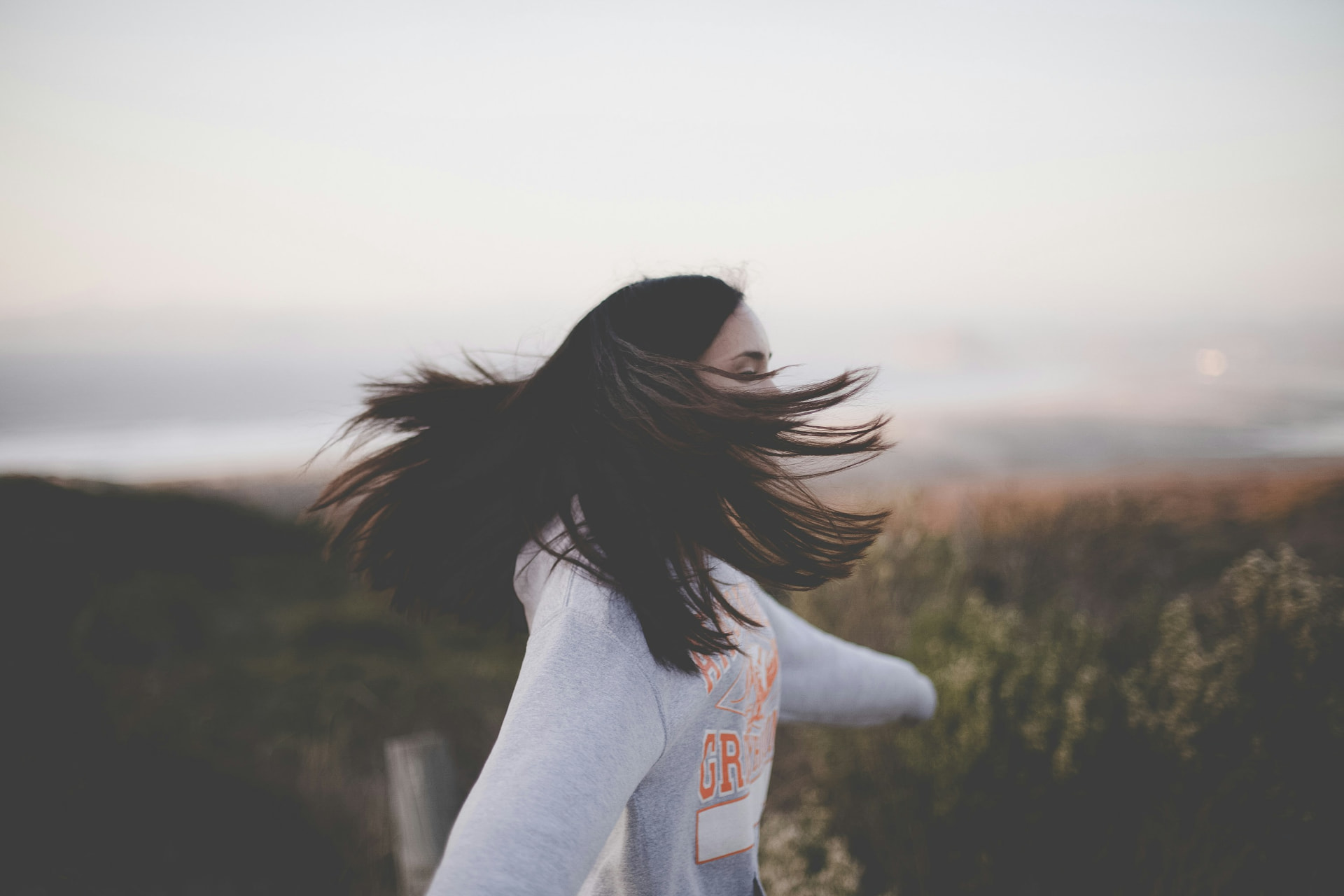A young woman spinning in a field at dusk, hair flying.