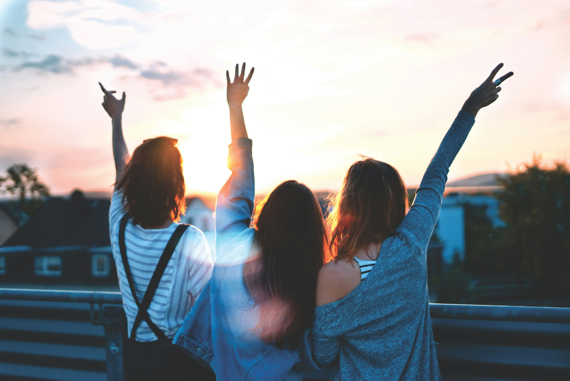 Three young women silhouetted against a sunset, arms raised.