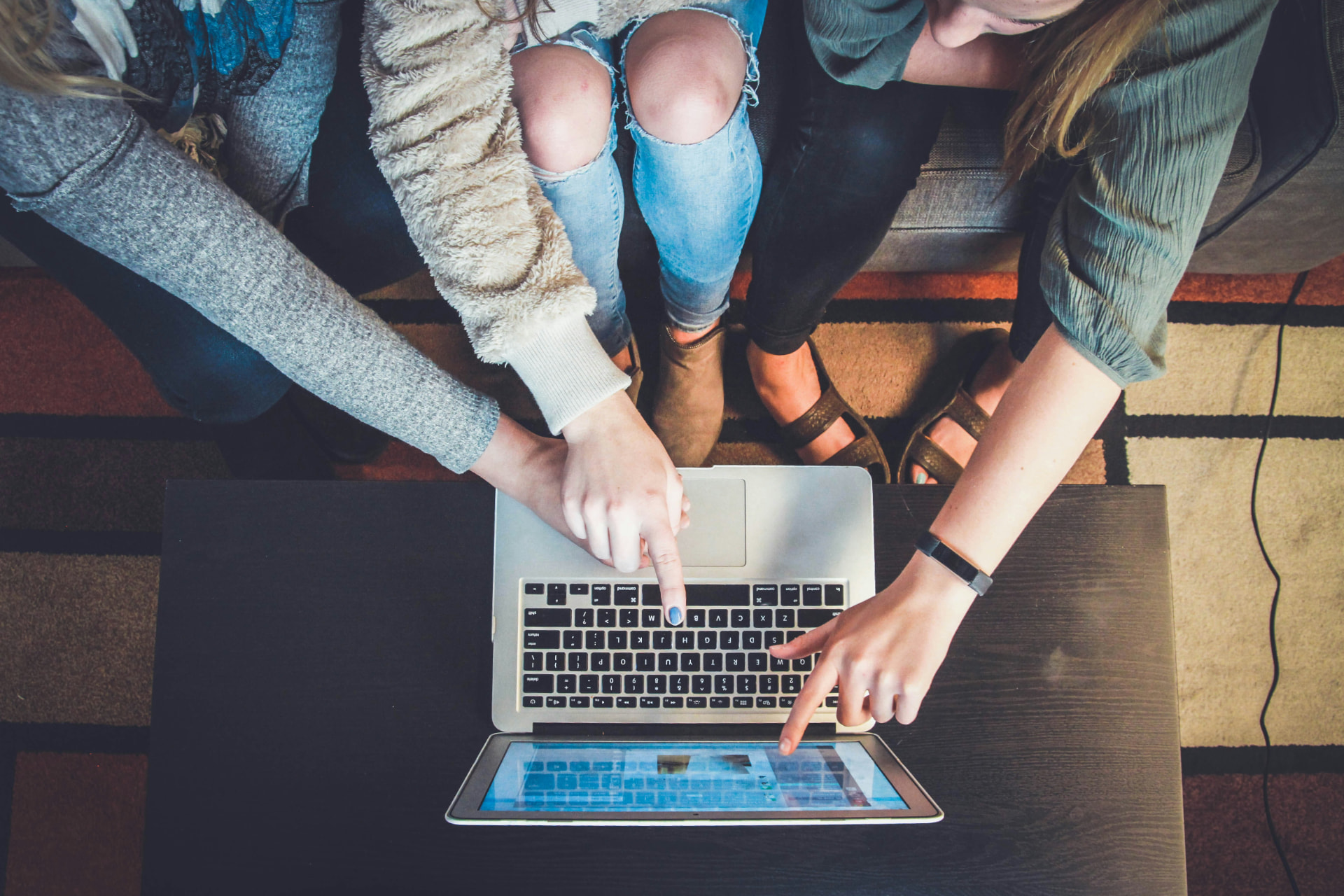 Overhead view of three young women pointing at a laptop and tablet on a table.